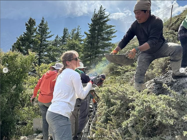 Man standing on a short cliff hands a woman a metal plate filled with something undiscernible